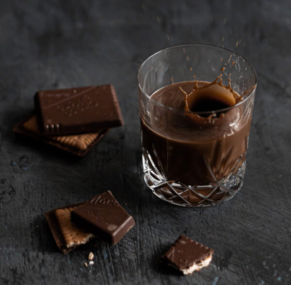 Cark chocolate flavored coffee in a glass next to bars of dark chocolate