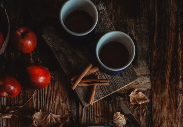 2 cups of French apple crumble cake flavored coffee next to two apples and 4 cinnamon sticks