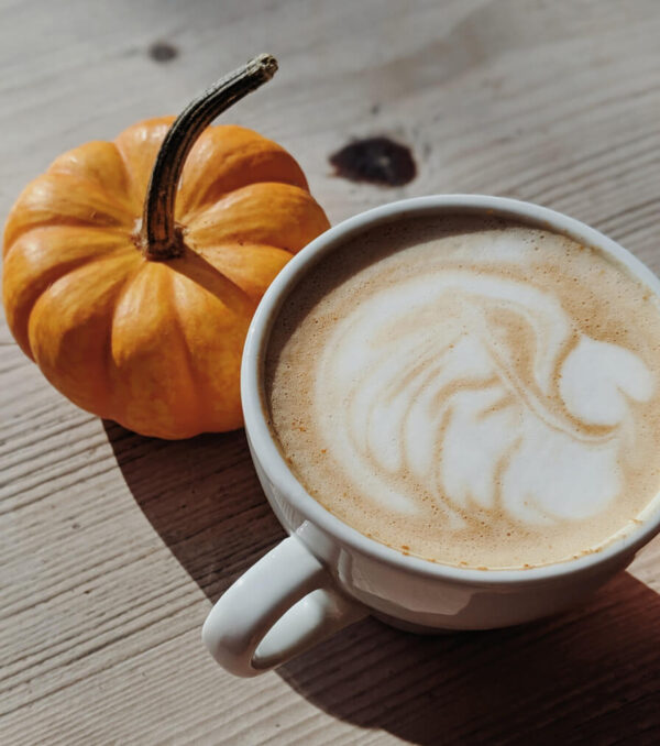 Pumpkin spics flavored coffee in a cup next to a mini pumpkin
